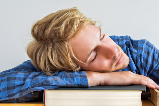 guy with books. a young guy with short blond hair and a blue shirt lies on a stack of books, close-up, reading concept