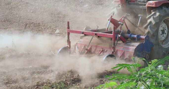 close up of the tractor plowing a field. The tractor is pulling a plow attachment that is turning over the soil. 