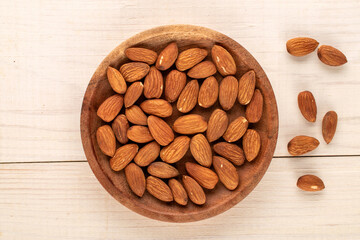 A small amount of roasted almonds with a wooden saucer on a wooden table, macro, top view.