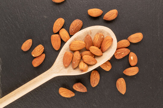 Several roasted almonds with wooden spoon on slate stone, macro, top view.