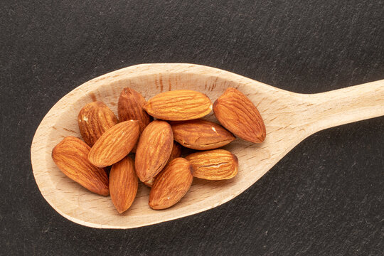 Several roasted almonds with wooden spoon on slate stone, macro, top view.