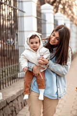 A young happy dark-haired woman carries her one-year-old daughter in her arms while walking.A family concept.Happy motherhood.