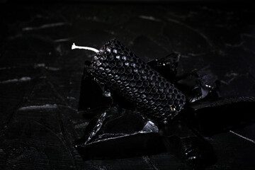 A candle made of black wax lies on the background and stone of black color.