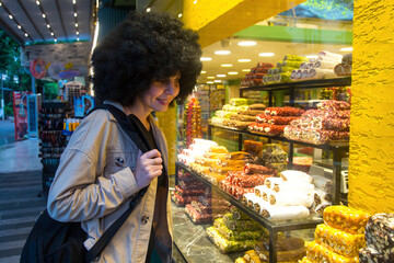 A girl with curly hair near a bright store window with bag on her shoulder