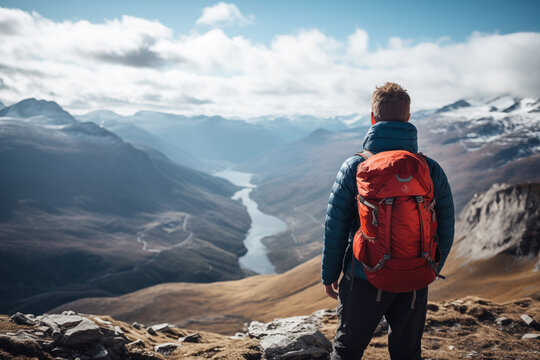 A hiker stands atop a mountain, gazing at a breathtaking vista. Silhouetted cliffs, summits, and valleys paint a stunning landscape.