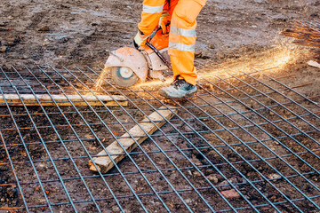 Builder cutting steel mesh with petrol-powered steel saw and creating a lot of sparks