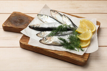 Fresh raw sprats, lemon and dill on light wooden table