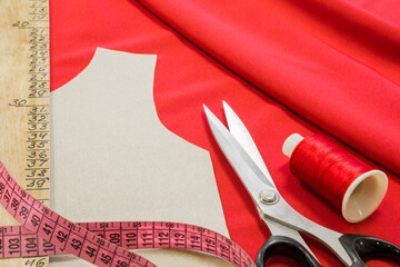 Fototapeta premium Scissors, measuring tape, ruler, contour template, thread spool on bright red fabric background. Sewing items preparation. Closeup.