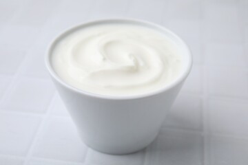 Delicious natural yogurt in bowl on white tiled table, closeup