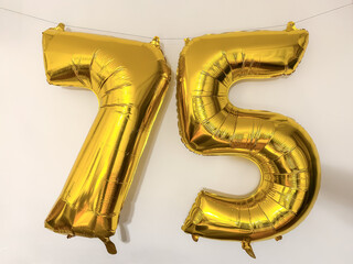 Gold foil balloons in the shape of the number 75, seventy-five hung on a thread.