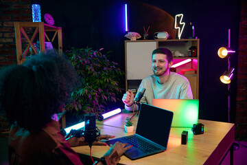 Young people, man and woman, influencers sitting at table with microphone and laptops, talking, recording online interview, podcast. Concept of online communication, modern technology, mass media