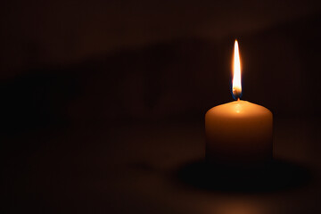 A wax candle is burning on a dark background. Flame of one candle at night close-up. Copy space