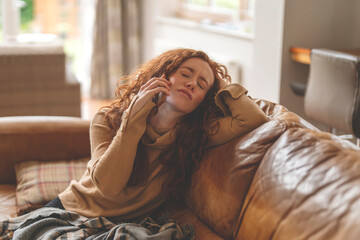 Sad and annoyed young redhead woman in brown shirt and using a mobile phone, listening to favorite...