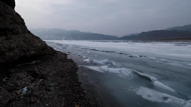 Harsh rocks and Mountain lake covered with ice, snow and hummocks in early spring. Bartogay reservoir in Kazakhstan.