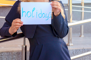 happy girl holding paper with the words holidays. Concept School holidays,graduation. girl in a uniform. pupil, learner, scholar. happy schoolgirl