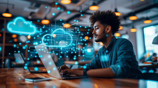 A focused young man engages with cloud technology graphics on a laptop at a modern workspace. - Powered by Adobe