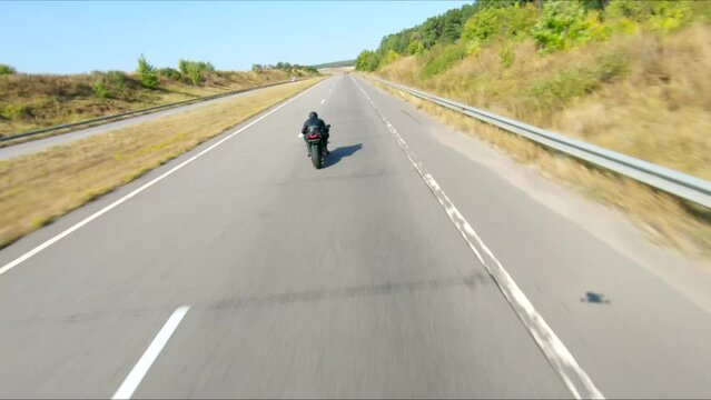 Aerial shot of man riding fast on modern sport motorbike at highway during summer day. Motorcyclist racing his motorcycle on country road. Guy drive bike during trip. Concept of freedom and adventure