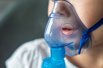 Close up view of little girl are sitting and holding a nebulizer mask leaning against the face,...