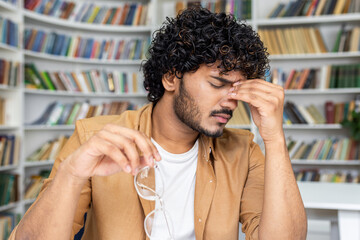 A young man with curly hair appears stressed and holds his head in pain, showing signs of a...