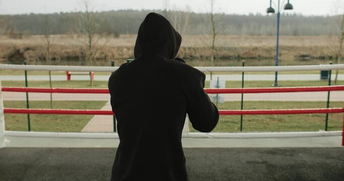 Sport work out motivation, medium shot of athlete man boxing outside on the outdoor ring. Healthy fit man boxing training