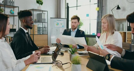 Business people team colleagues sitting at office table and getting business statistics with charts from main man manager during meeting in company - Powered by Adobe