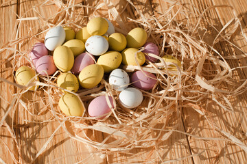 Multi-colored chocolate decorative eggs with dry corn on a wooden background. Happy Easter background. Top view
