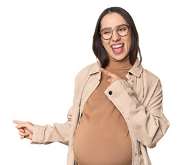 Pregnant young Caucasian woman showcasing maternity on studio background pointing with forefingers...