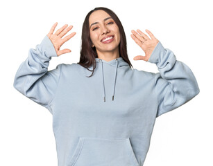 Modern young Caucasian woman portrait on studio background showing number ten with hands.