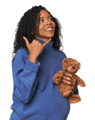 Expecting African American with teddy bear showing a mobile phone call gesture with fingers.
