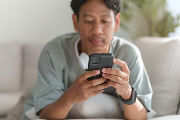 Young Asian man resting on sofa and using smart phone.