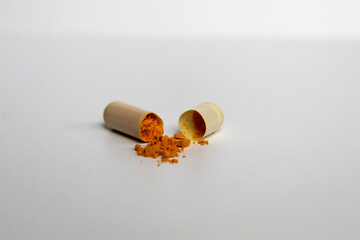 Opened capsule with yellow turmeric powder filling inside. Isolated on white background