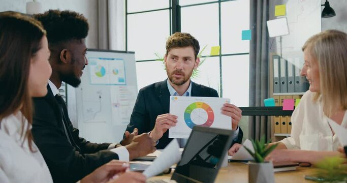 Confident man main director explaining results of statistic researches to attentive mixed races subordinates in office room. Concept of collaboration.