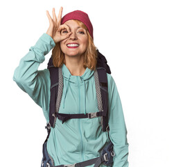 Middle-aged Caucasian woman with hiking gear excited keeping ok gesture on eye.