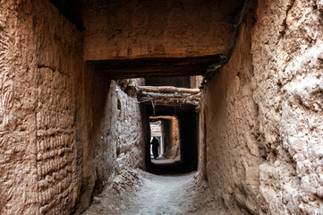 Woman walking through a covered alley in the historic village of Mhamid, Morocco - 750700515