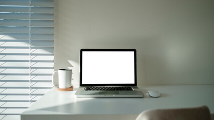 Laptop with blank screen and cup of coffee on wooden table in bright office.