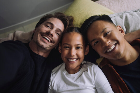 Directly above portrait of smiling gay couple lying down with daughter at home