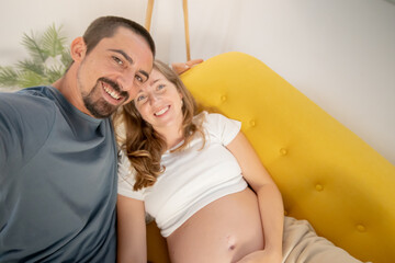 A pregnant woman and her husband are photographing themselves on the cell phone at home. High quality photo