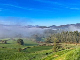 Natural landscape in a sunny sunrise with fog in a natural park surrounded by forests and green meadows in northern Spain.