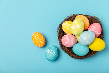 Easter eggs in the nest with mimosa flowers on a bright yellow background. Easter celebration concept. Colorful easter handmade decorated Easter eggs. Place for text. Copy space.