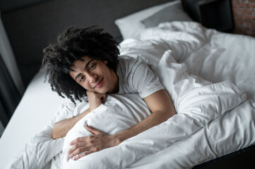 Young man lying in bed and looking relaxed