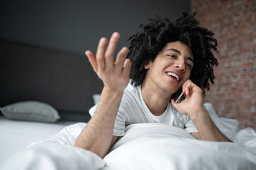 Fototapeta na wymiar Young man lying in bed and talking on his phone