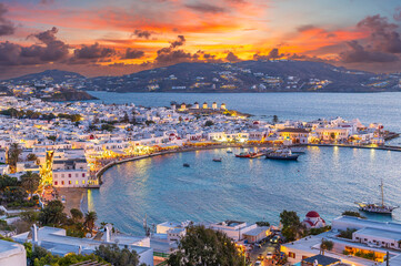 Naklejka premium Embrace the warm hues of sunset in Mykonos Town Chora, where the Aegean Sea's azure waters reflect the vibrant life of this iconic Greek island.