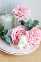 Cute edible teddy bear toy made of white chocolate with fresh peonies and candles on the backgrounds. Gift for a baby