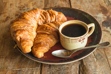 Traditional french breakfast: cup of coffee and hot croissants on a wooden background