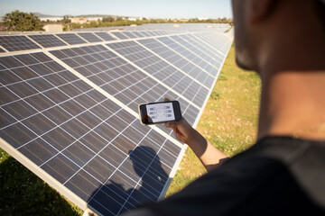Male engineer programming solar panels through smart phone app at power station