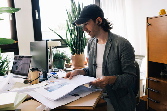 Male architect analyzing blueprint while sitting at desk in home office