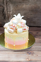 Tender pink birthday cake with melted white chocolate, fondant crown, meringues and marshmallows on rustic background