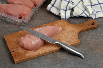 Filet de poulet cru avec un couteau sur une planche à découper avec une barquette en plastique de filets de poulet crus