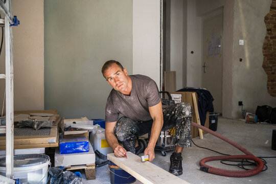 Portrait of male carpenter marking with pencil on plank in room at apartment