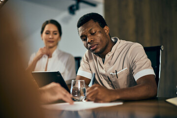 A black male doctor signed a contract during the meeting with his colleagues.